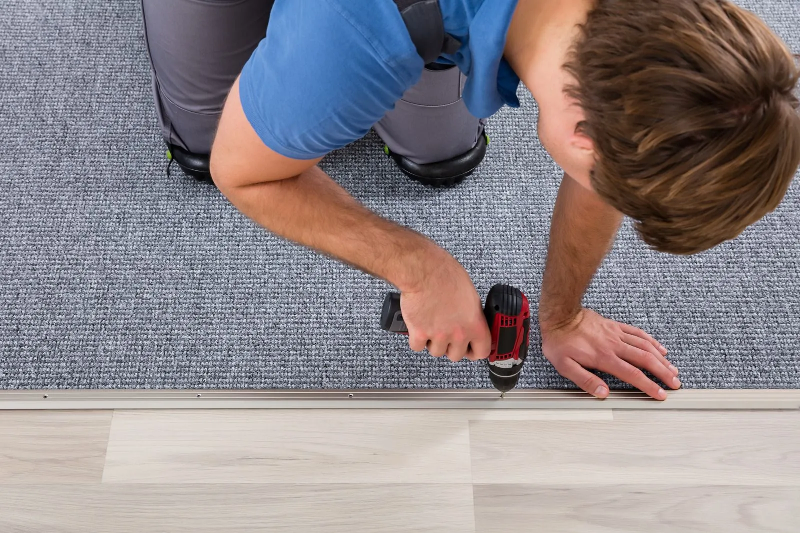 "Worker installing carpet to laminate transition strip using a power drill"