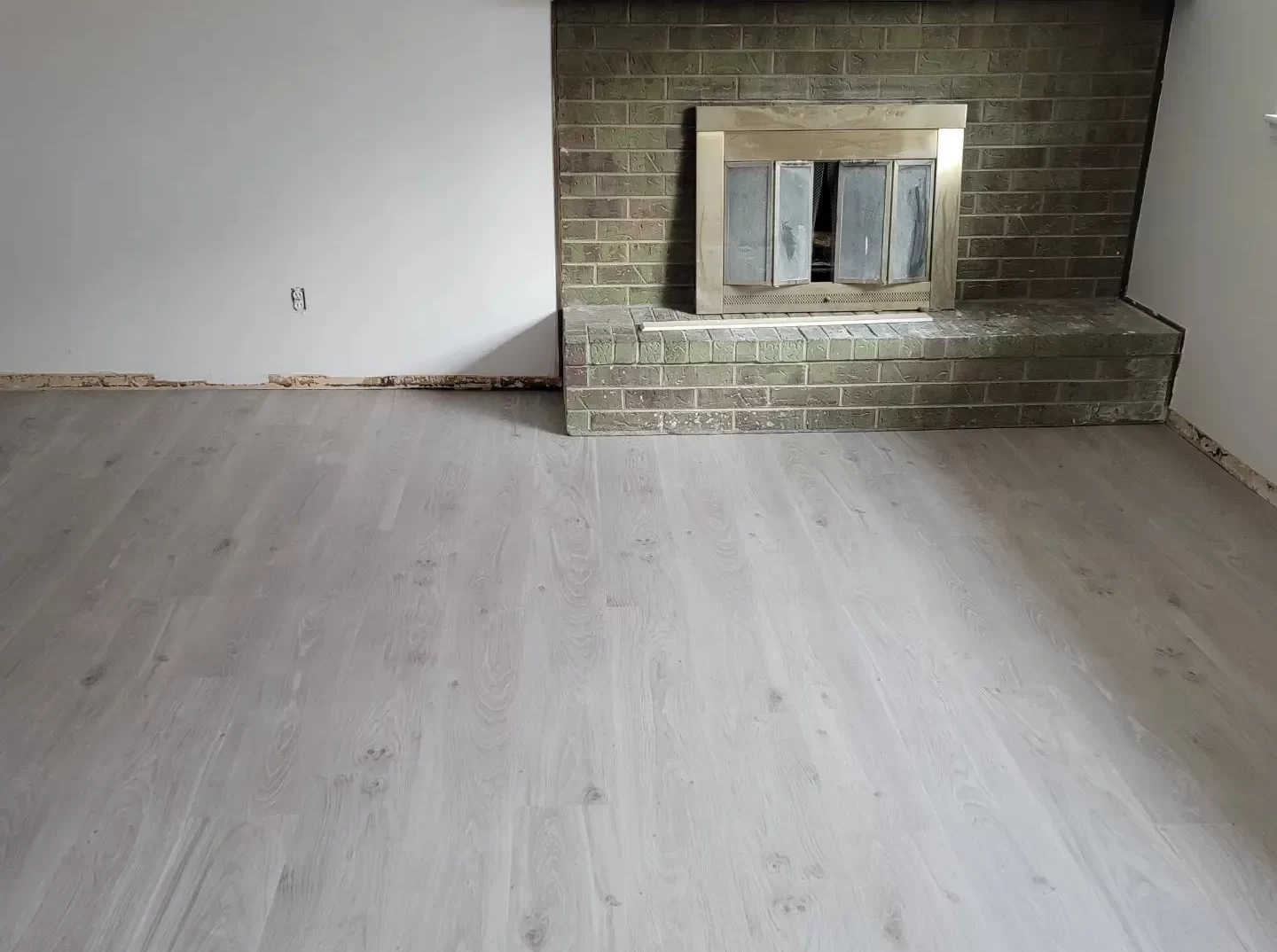 "Light gray laminate flooring in living room with brick fireplace"