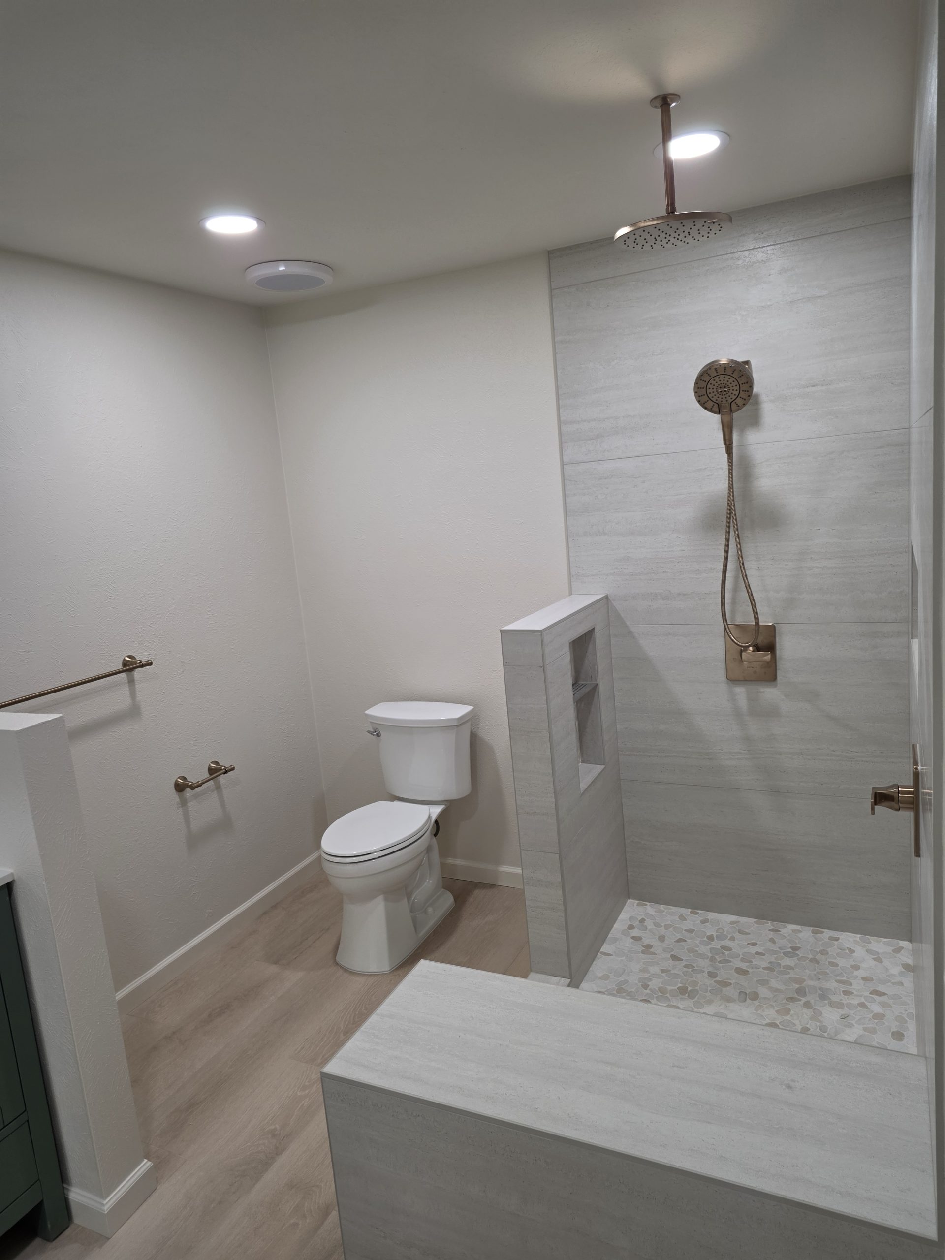 Walk-in shower finished in travertine-look porcelain tile with a pebble mosaic accent band, in a Littleton, CO bathroom remodel