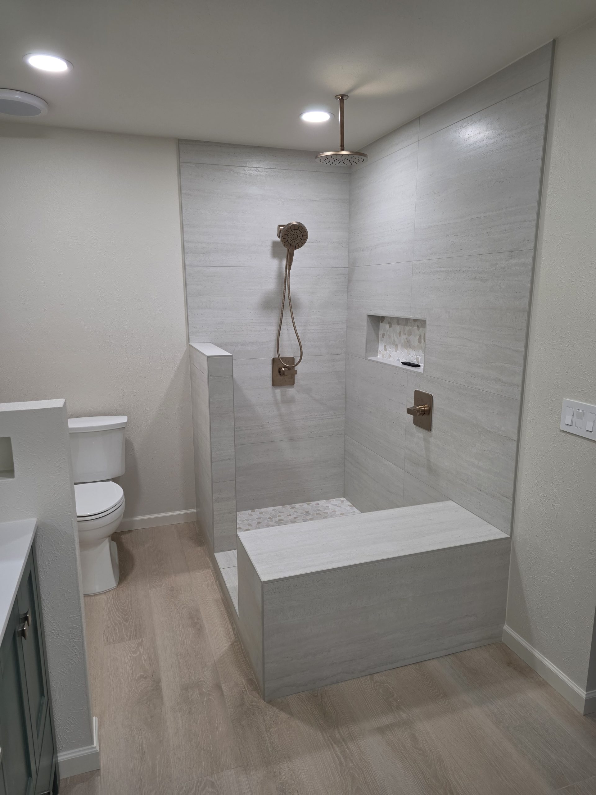 Low-curb walk-in shower with pebble mosaic niche and wood-look plank flooring in a Littleton, CO bathroom remodel