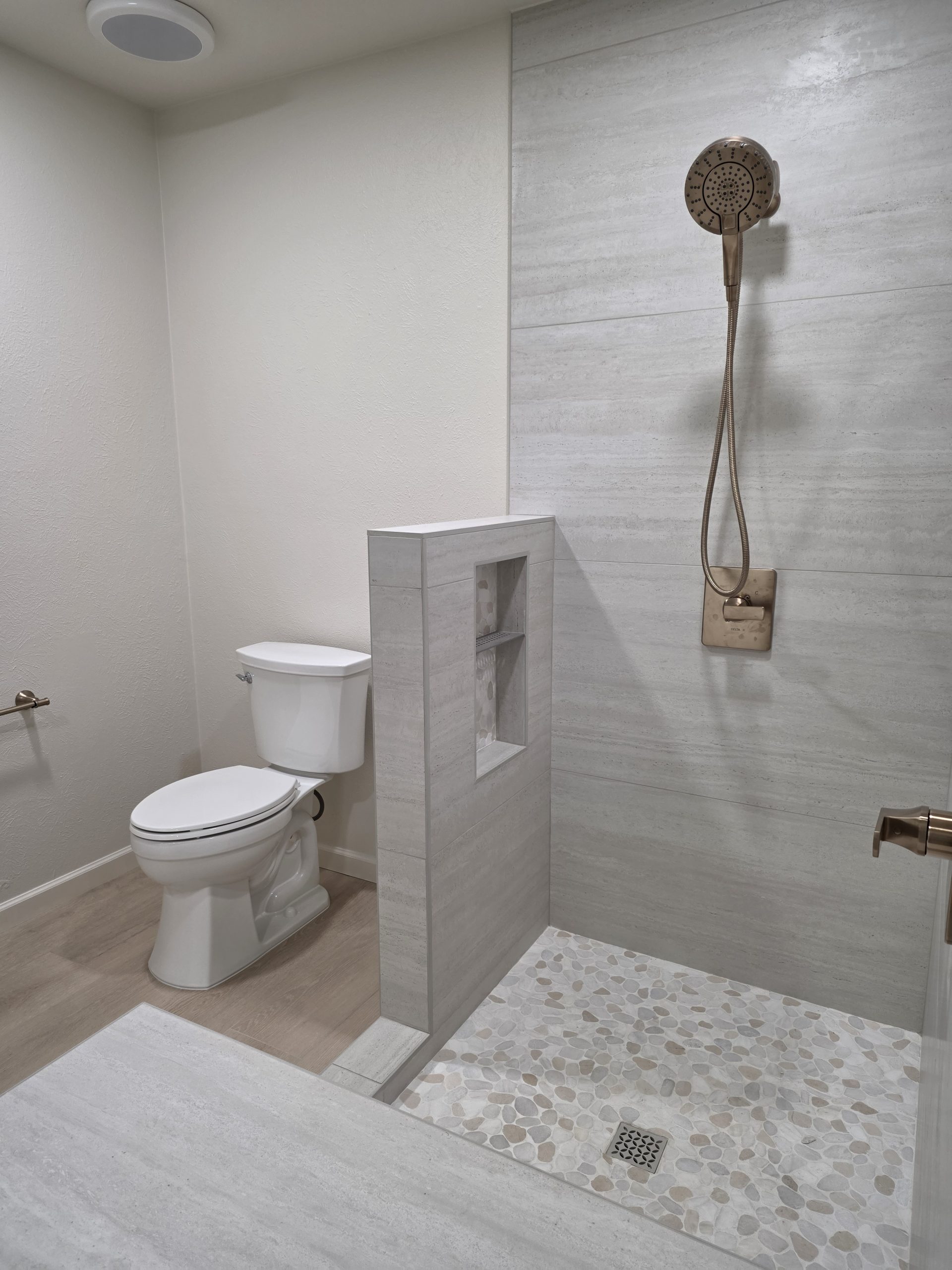 Wood-look plank flooring meeting tiled shower curb in a Littleton, CO bathroom