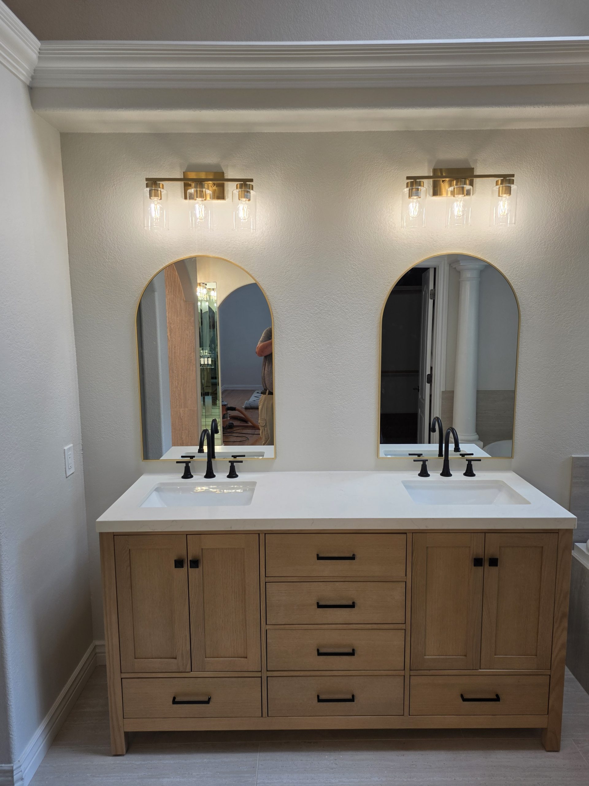 White oak double vanity with arched mirrors and brass sconces in a Highlands Ranch, CO master bathroom