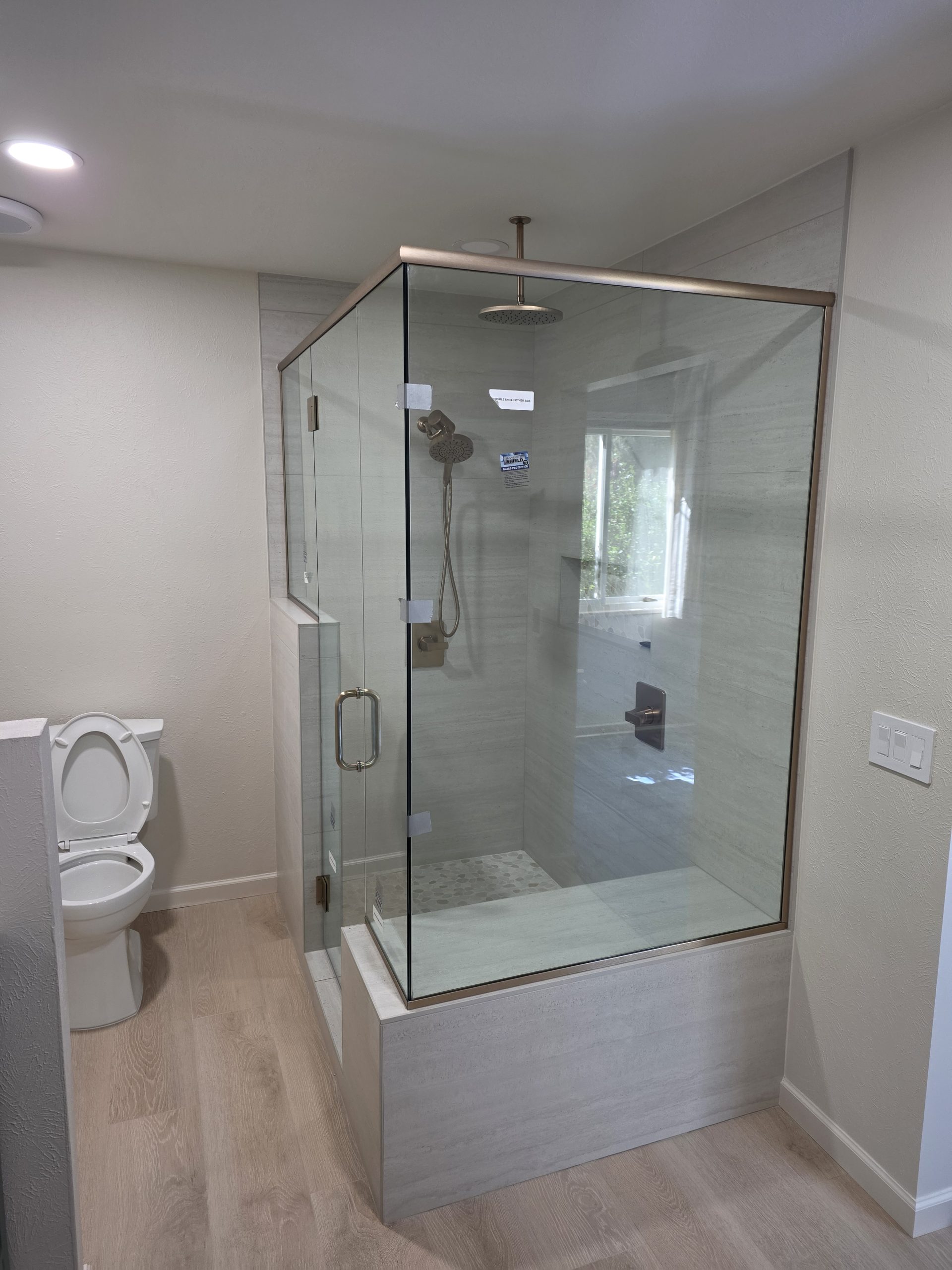 Frameless glass shower enclosure over travertine-look porcelain tile and a pebble mosaic niche, in a Littleton, CO bathroom remodel