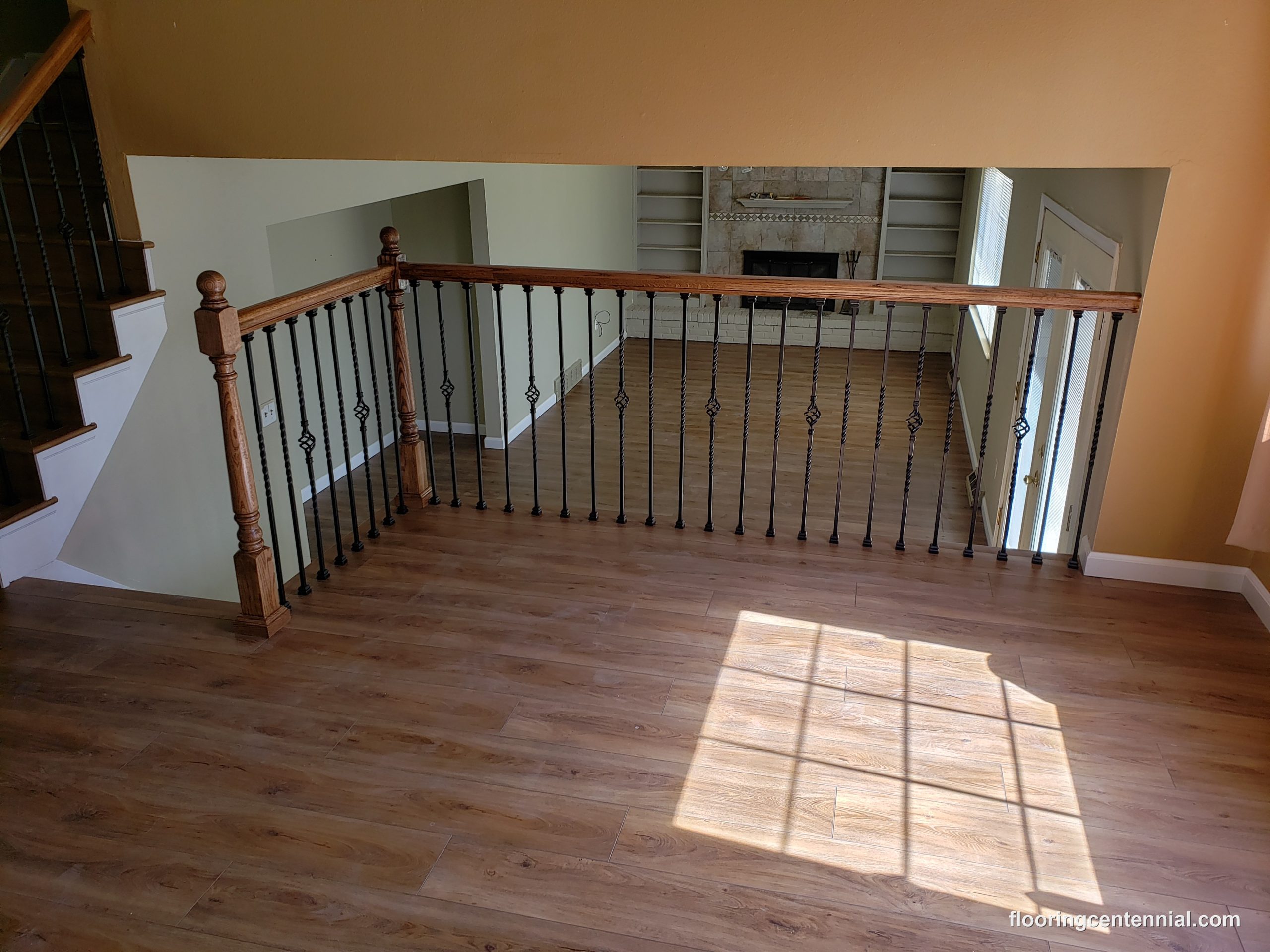 Open-concept great room with wood-look flooring and wrought iron stair railing overlooking a stone fireplace