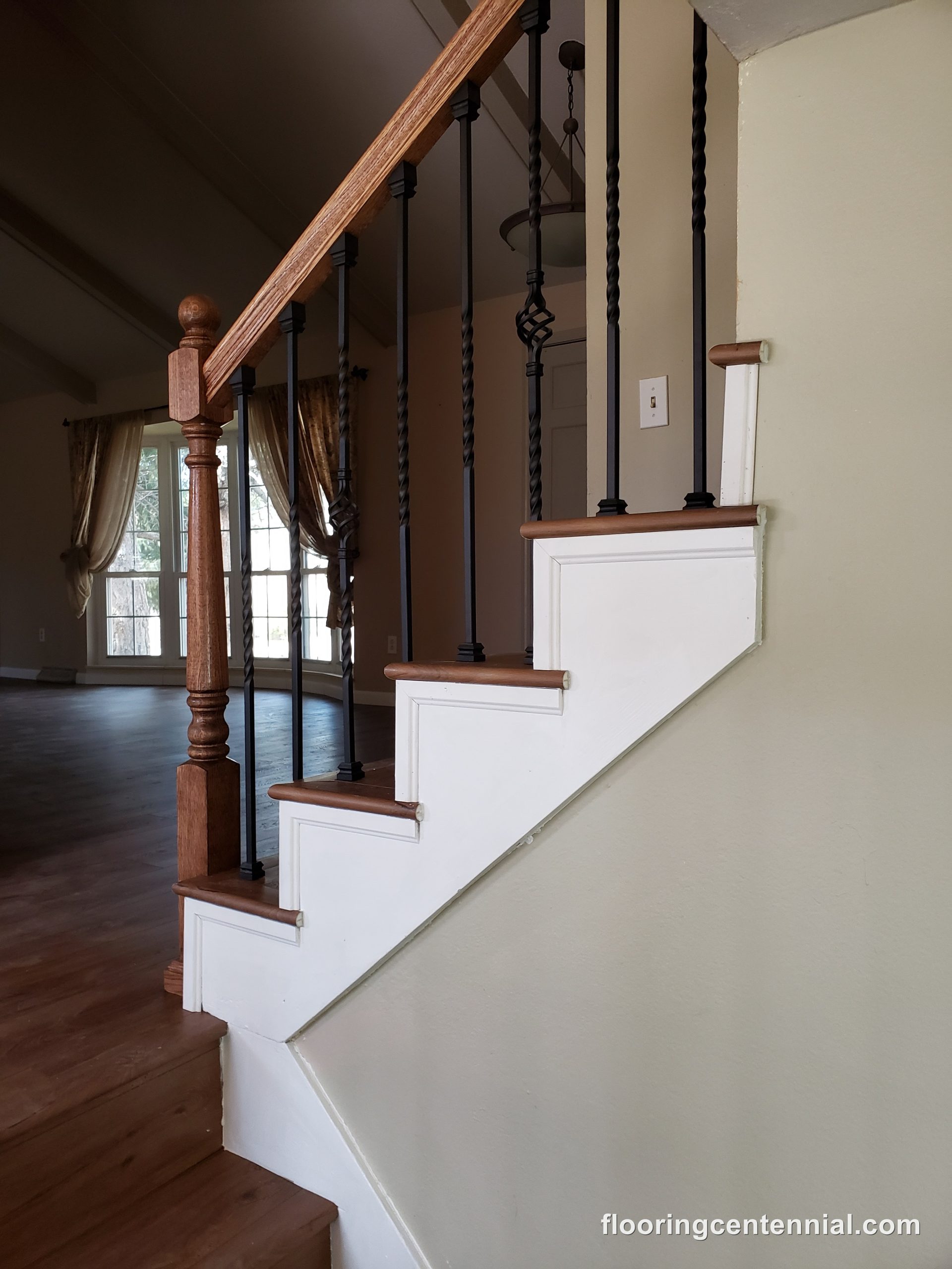 Vaulted staircase with oak railing overlooking a hardwood-floored living room
