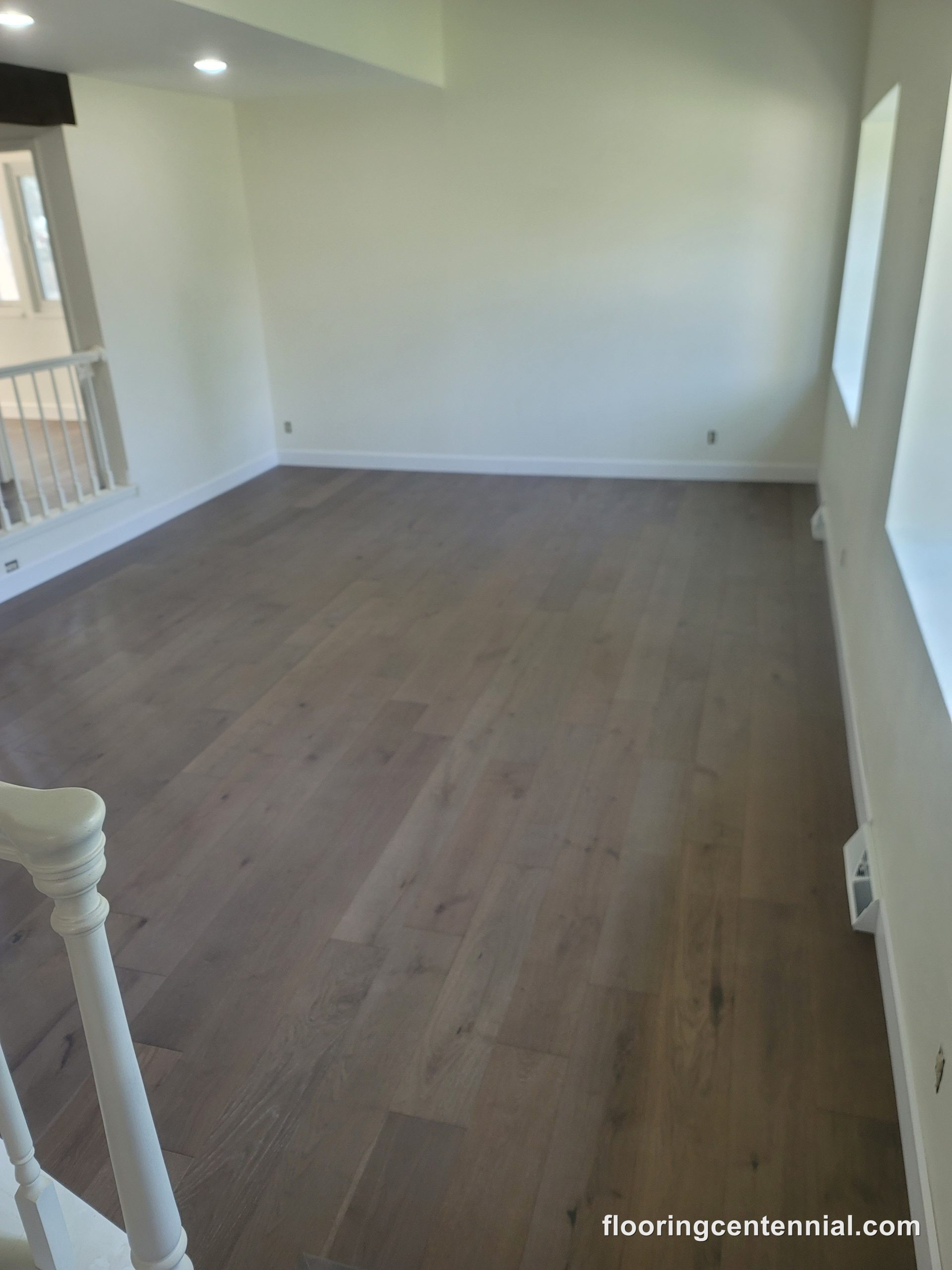 Open room with rich brown hardwood flooring and white staircase railing