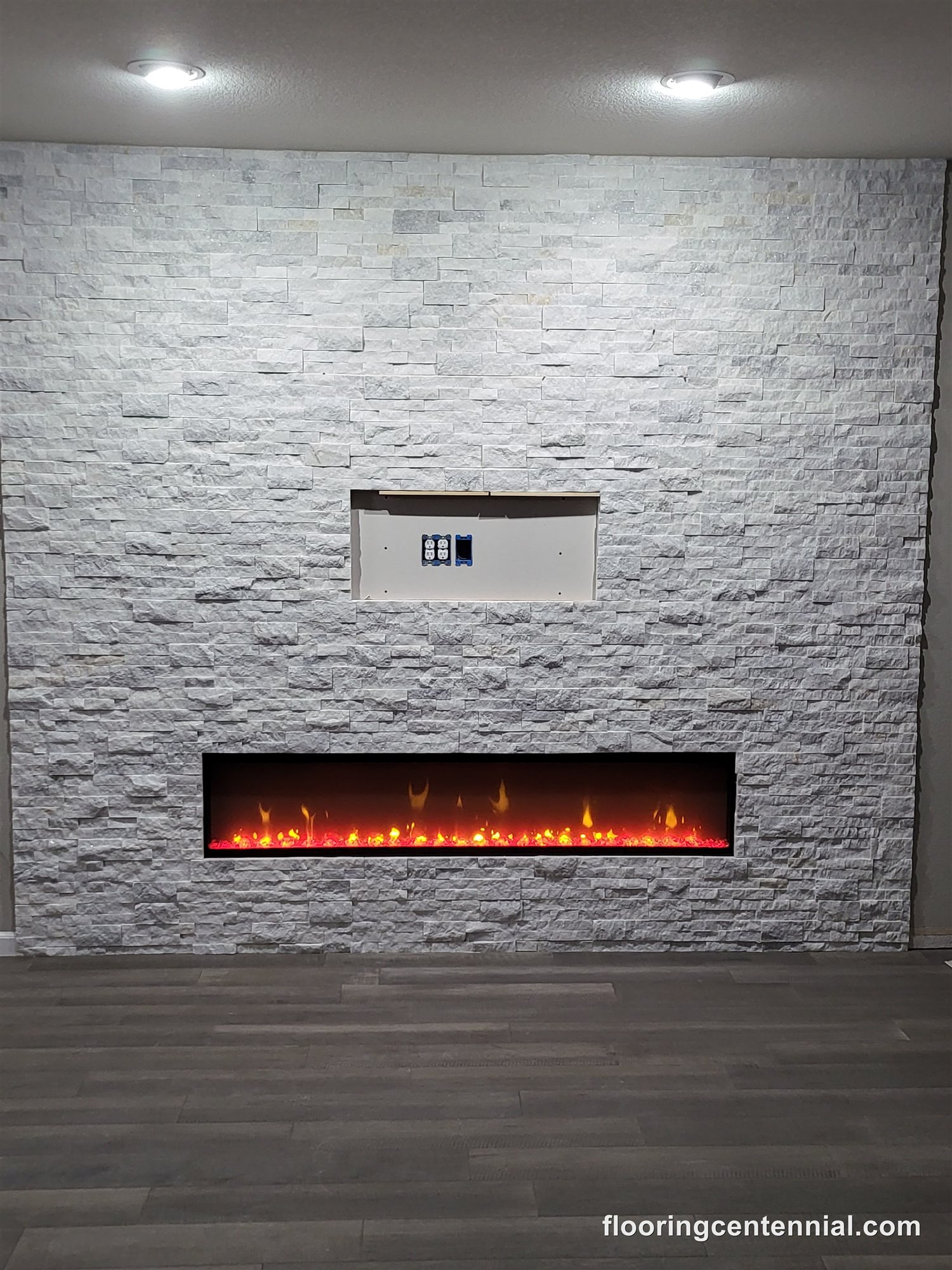 White stacked stone fireplace with linear insert and gray wood-look flooring