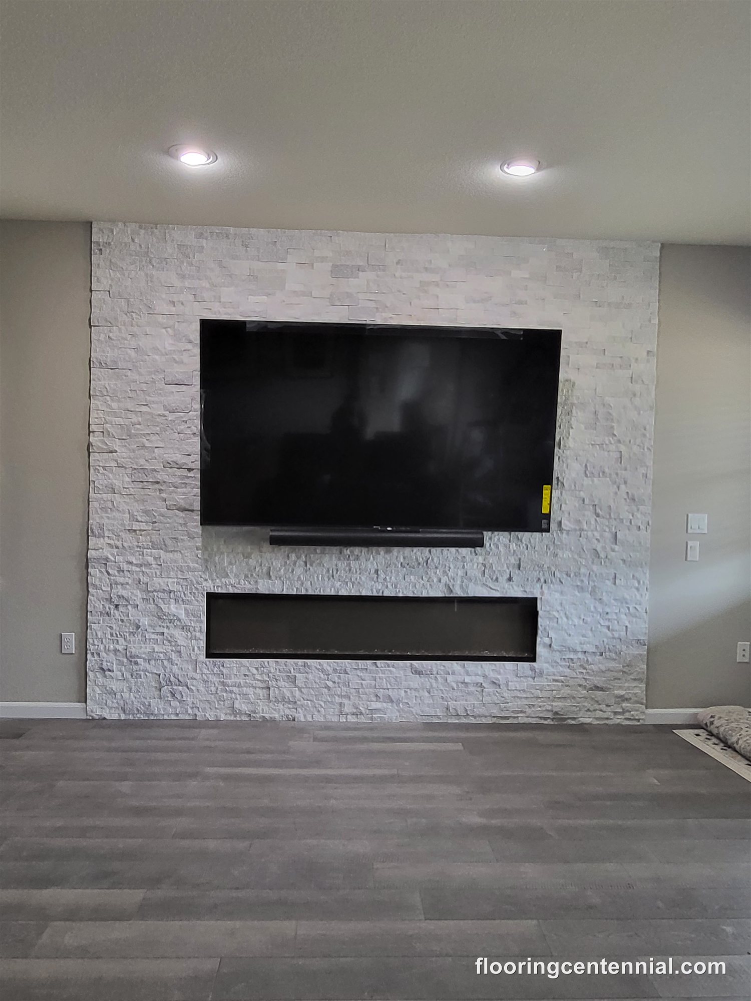 White stacked stone fireplace wall with mounted TV and gray wood-look flooring