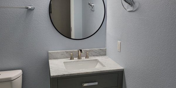 Powder room remodel with round mirror and tile flooring