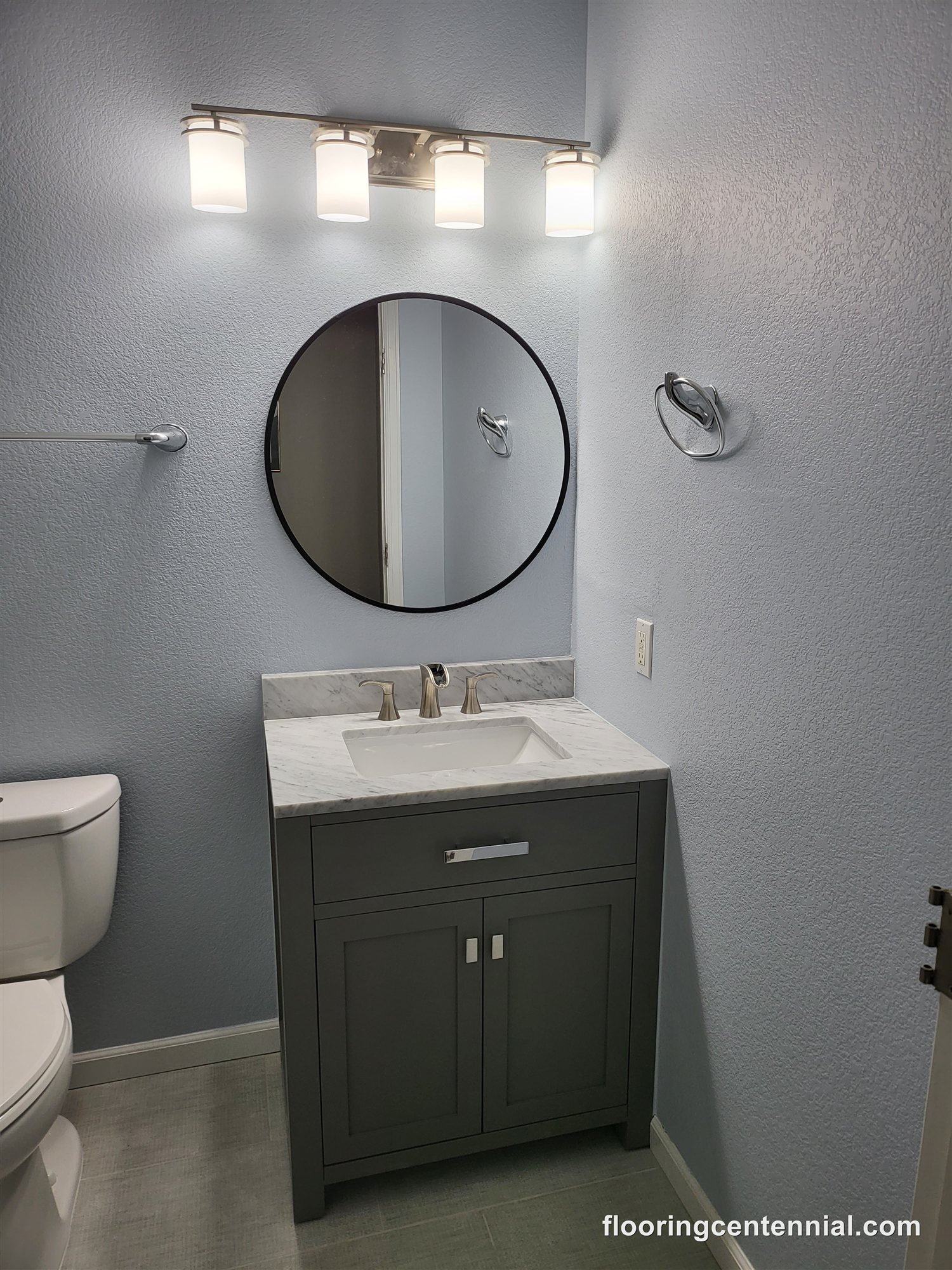 Powder room remodel with round mirror and tile flooring