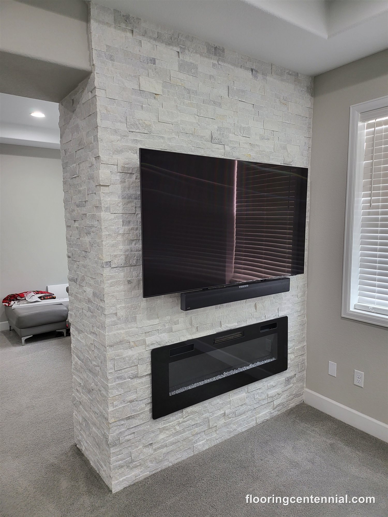 Stacked stone fireplace with mounted TV and soundbar in a finished basement