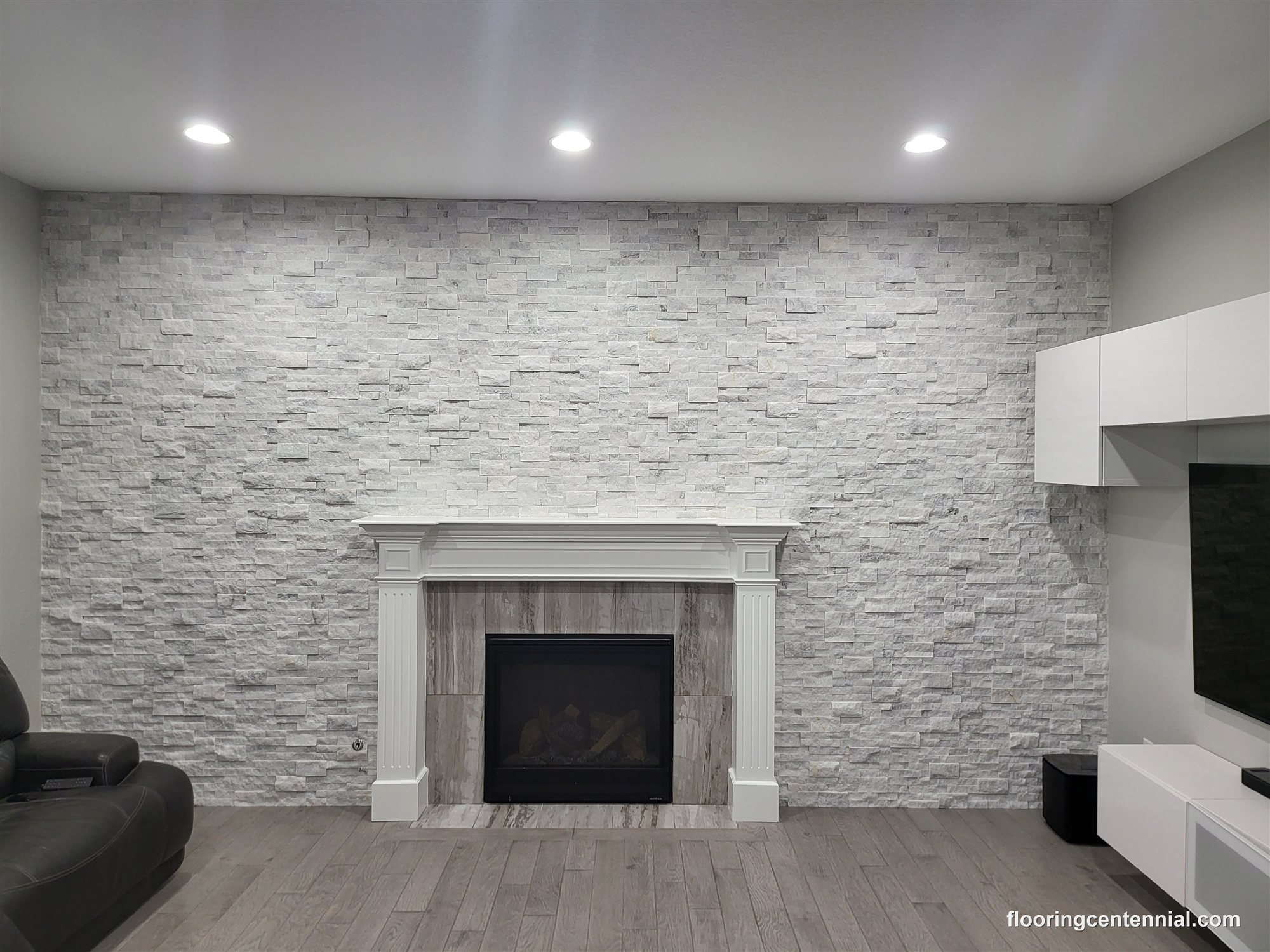 Stacked stone fireplace wall with mounted TV and gray hardwood flooring