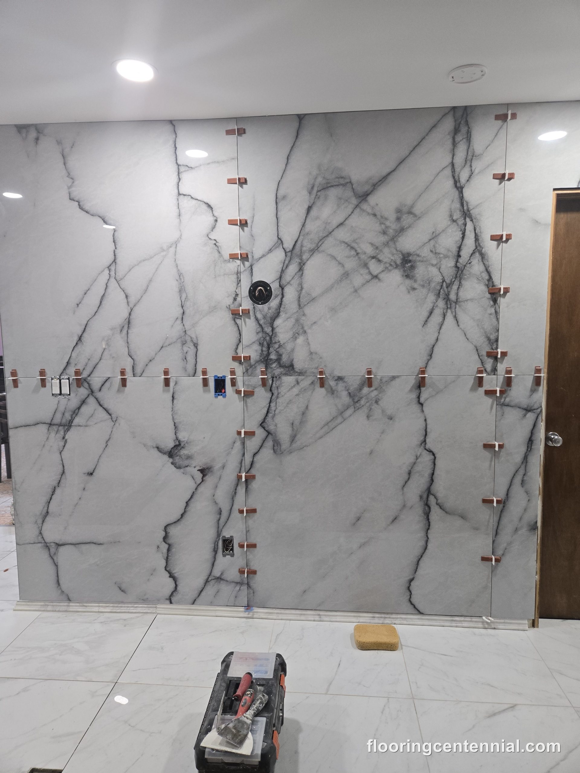 Marble-look tile being installed on a bathroom wall, spacers still in place