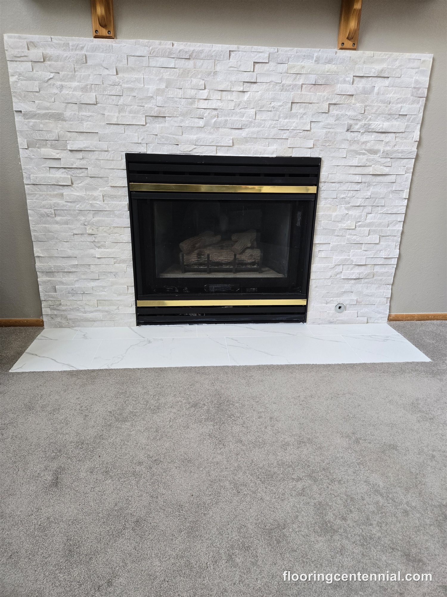 White stacked stone fireplace with brass trim insert and marble hearth