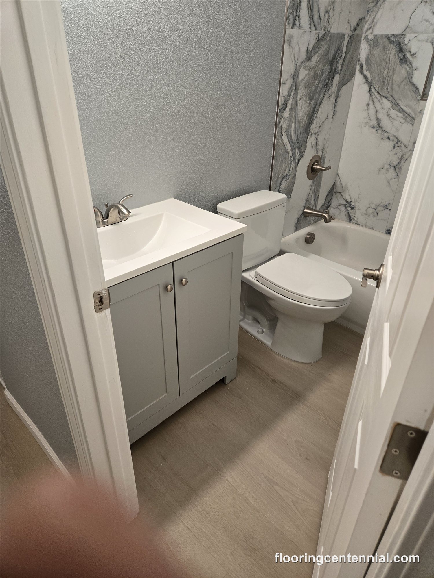 Bathroom remodel with marble-look tub surround and wood-look flooring
