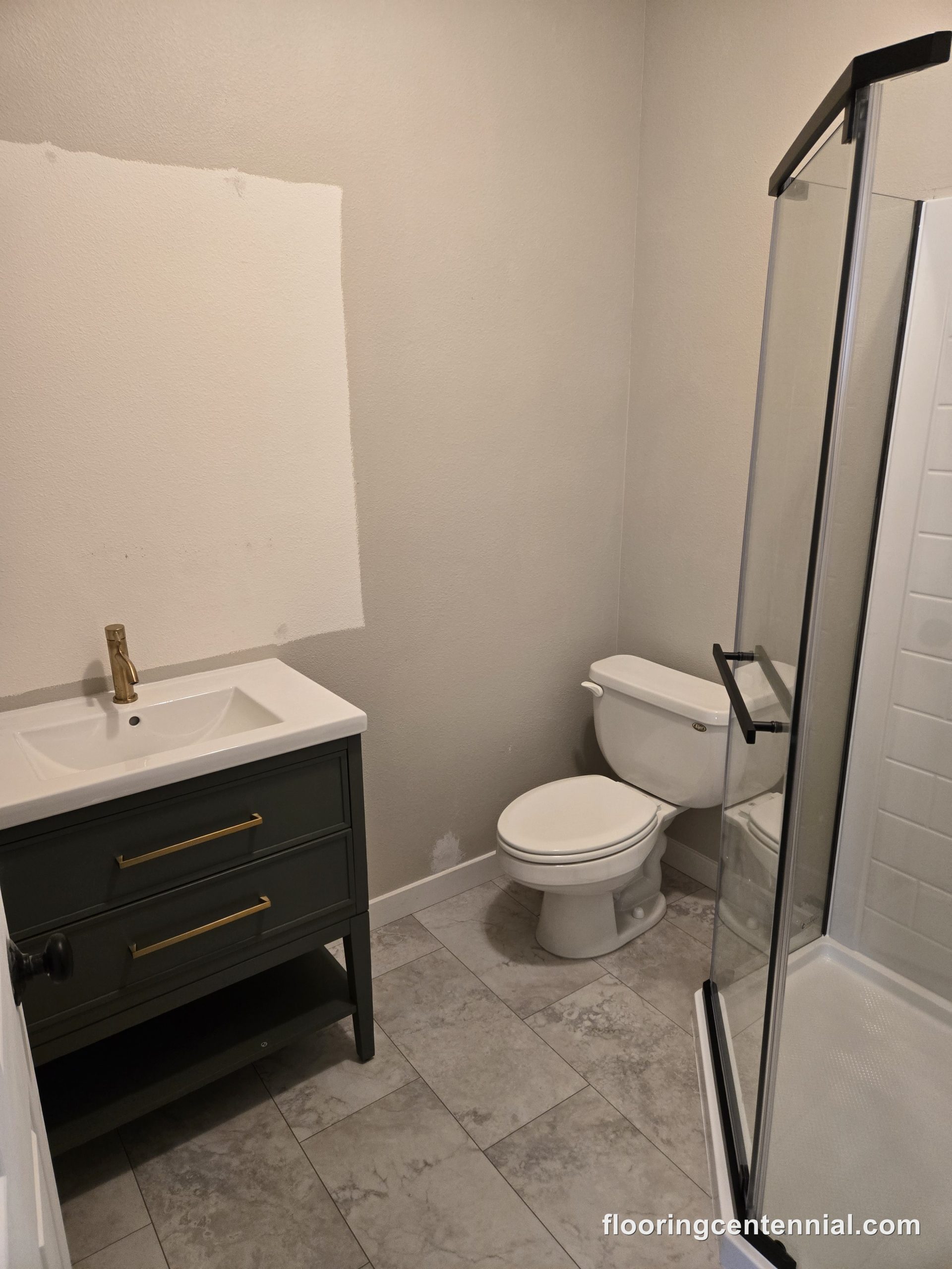 Bathroom remodel with dark green vanity, brushed gold fixtures, and tile flooring